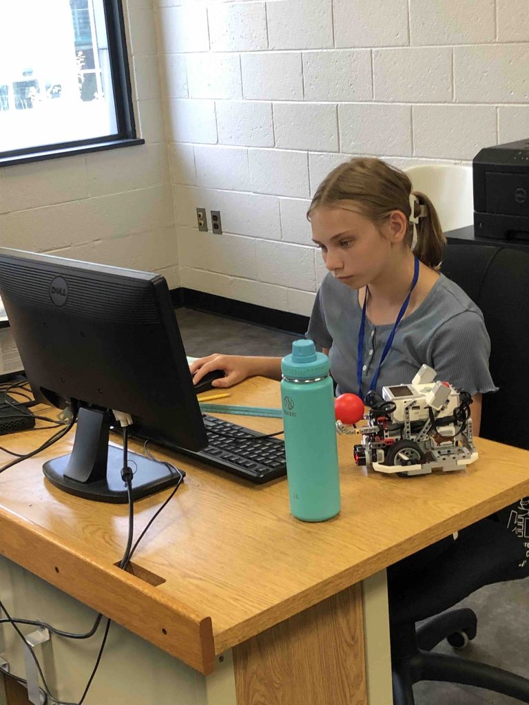 student working at a computer with a small plastic robot next to her on the table