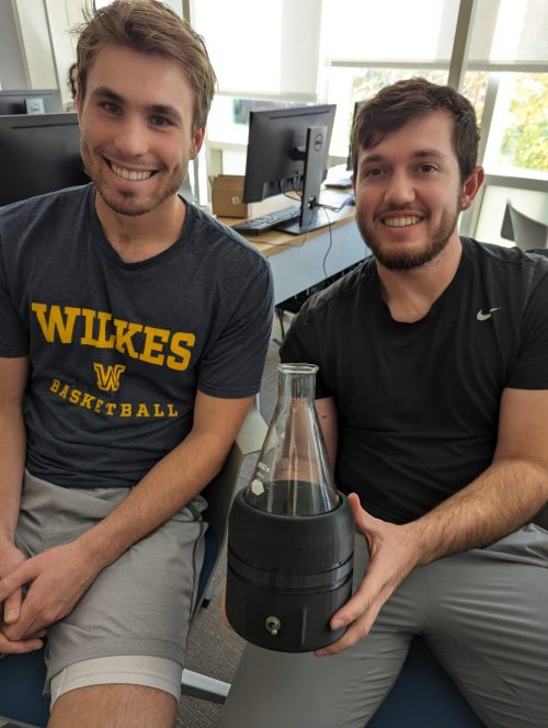 Product development students holding their invention, a stirring device.