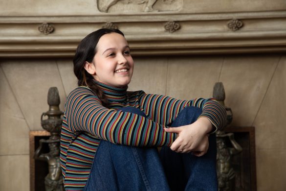 Picture of a young woman with dark hair in a striped turtleneck shirt sitting with arms wrapped around her knees