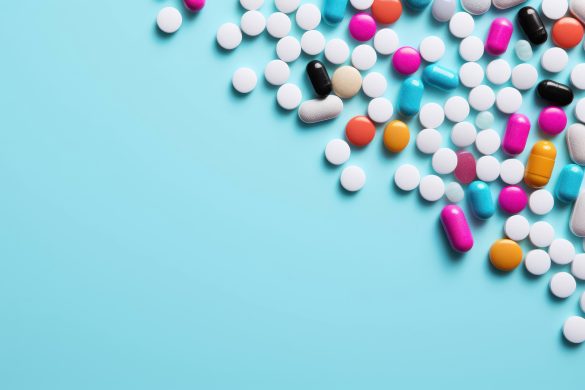 multi-colored pills and capsules scattered on a light blue background