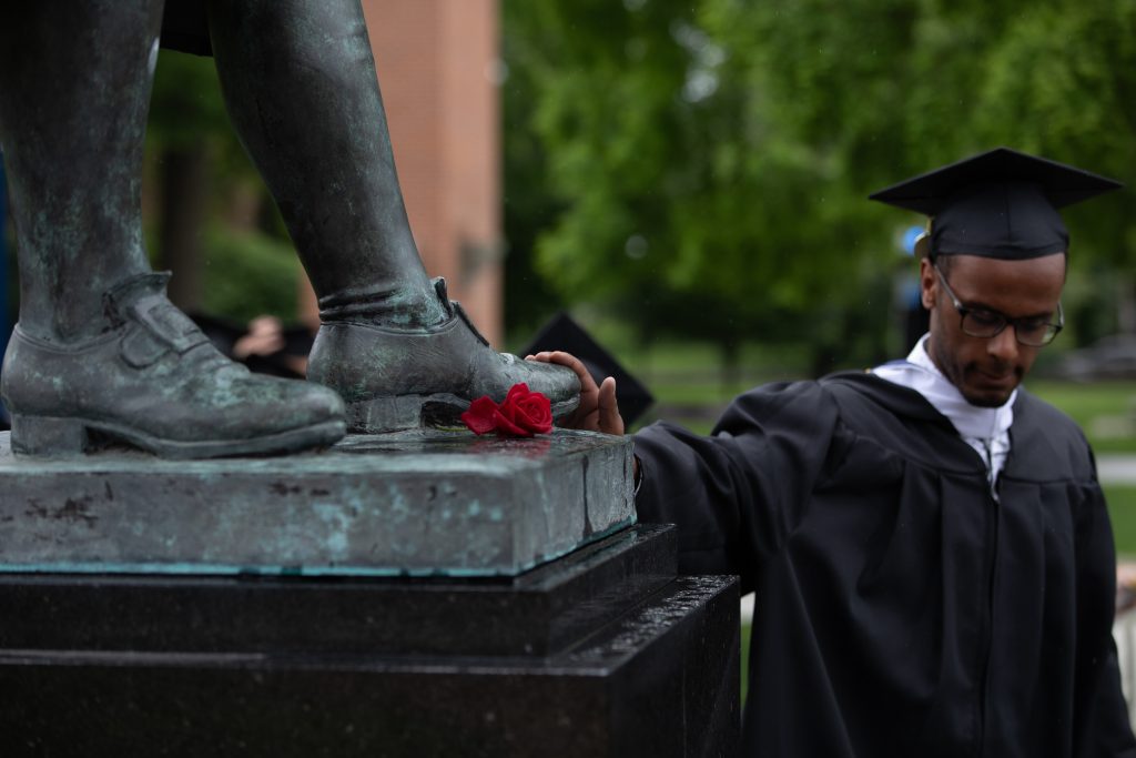 graduate touches the boot of the john wilkes statue for luck - a Wilkes tradition during the commencement procession 