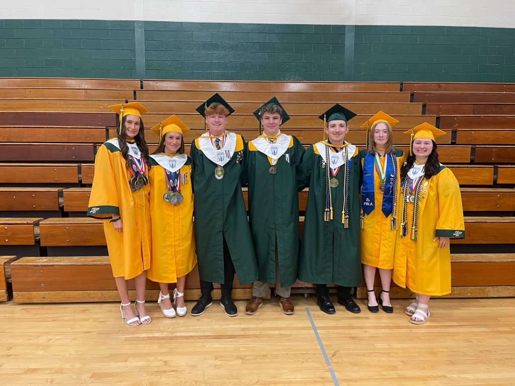 High school graduates wearing their caps and gowns standing in front of bleachers in the gym