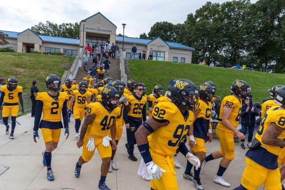 Wilkes football players run down the stairs toward the field