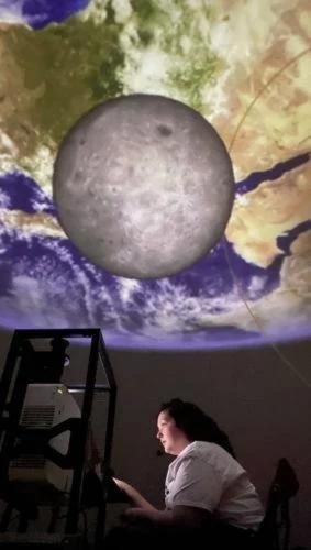 miquela langan in planetarium with projections of the earth and moon in the background