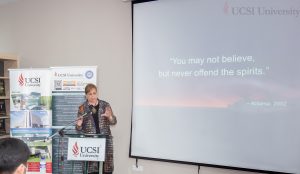 Woman lecturing behind a podium next to a screen