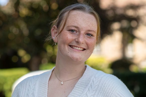 photo of young woman smiling with trees and a building in the background