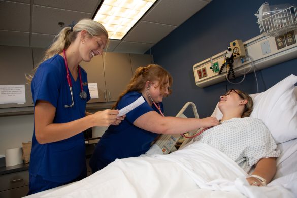 Two Wilkes nursing students working with a patient in a bed