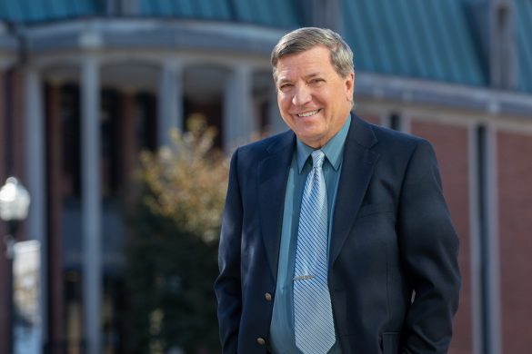 Photo of man in jacket and tie standing in front of the library at Wilkes