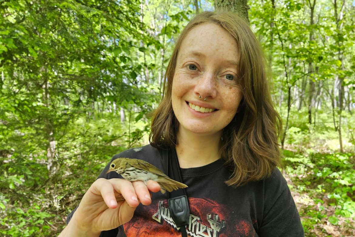 Amy Yanagitsuru in the woods with a bird perched on her finger